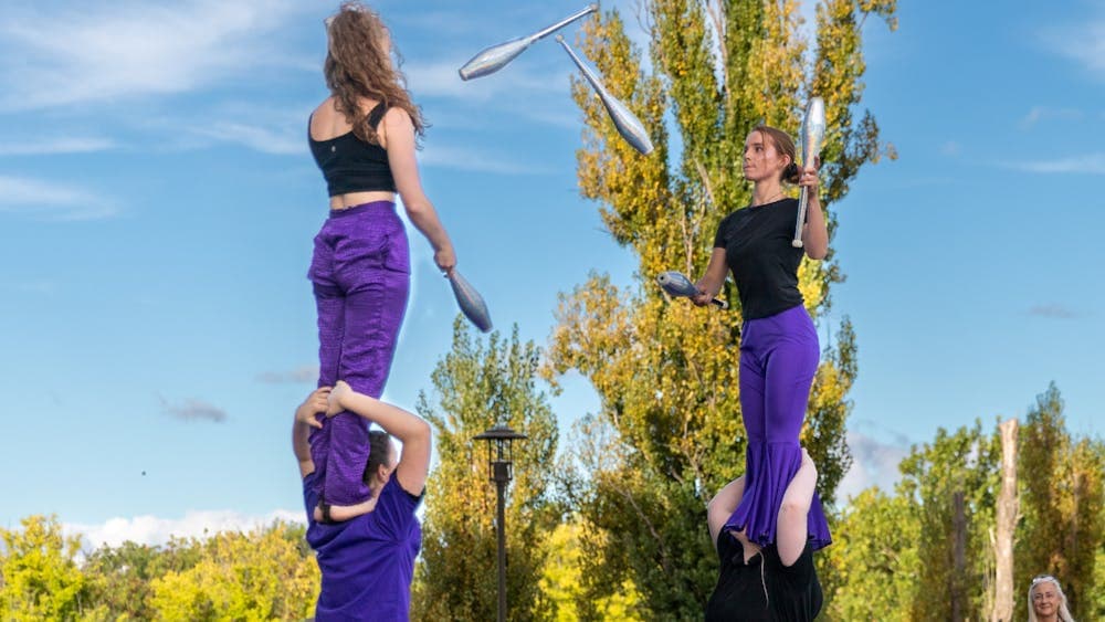 Warehouse Circus artists juggle to each other while balanced on shoulders