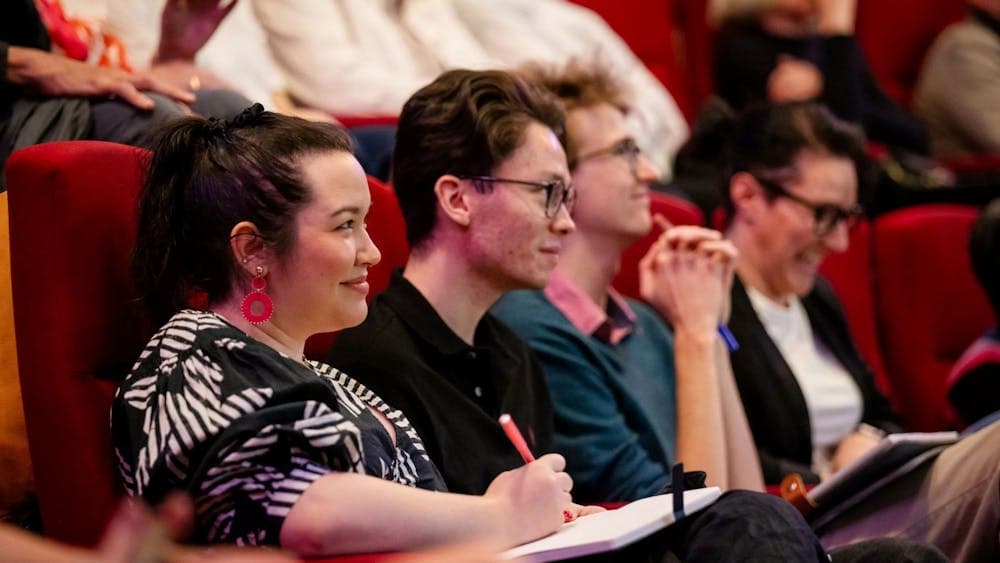 People sitting in a theatre smiling and listening to the speakers