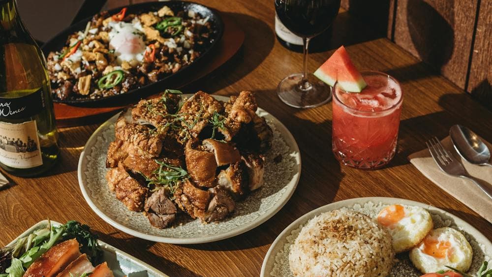 A wooden dining table filled with Filipino dishes including crispy pork belly, fried rice with eggs,