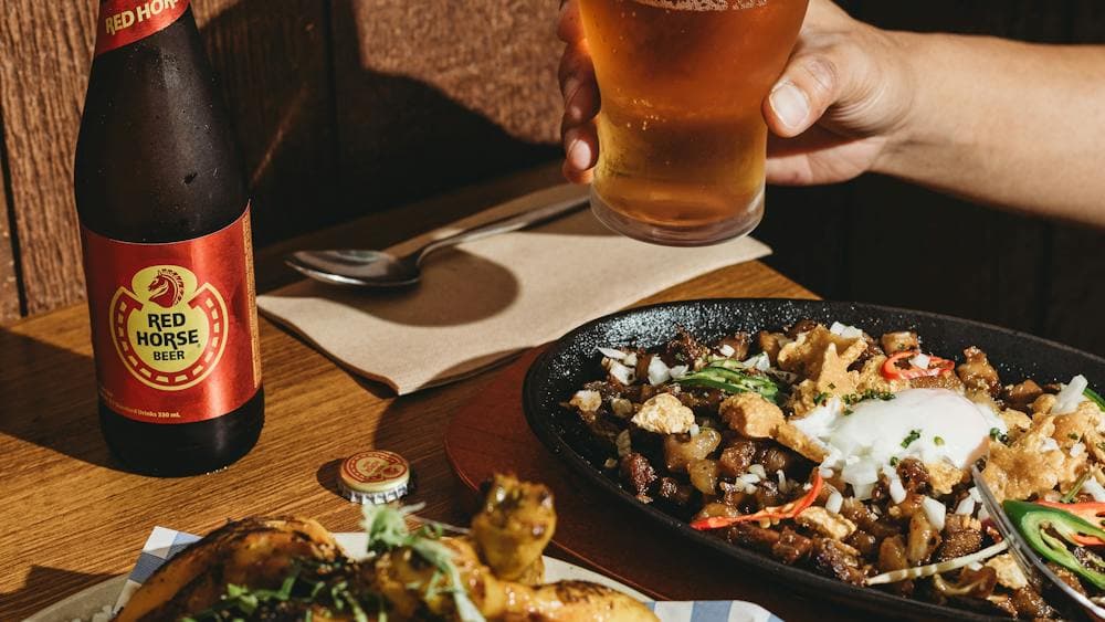 A table with Filipino dishes including grilled pork, sizzling sisig topped with an egg and chili, a