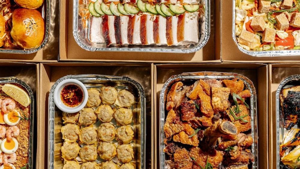 Assorted Filipino catering trays filled with roasted meats, buns, dumplings, seafood, salads and veg