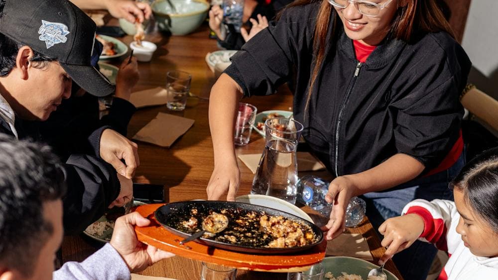 A group of people sitting around a dining table sharing Filipino dishes, with plates, bowls and drin