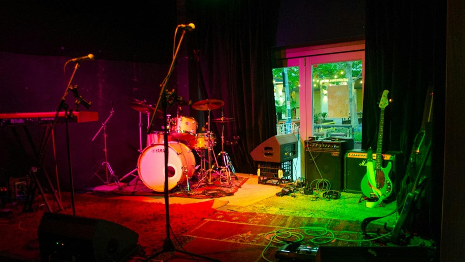 Image of a drumset, microphone, a couple of amps on a stage with red and green lighting.
