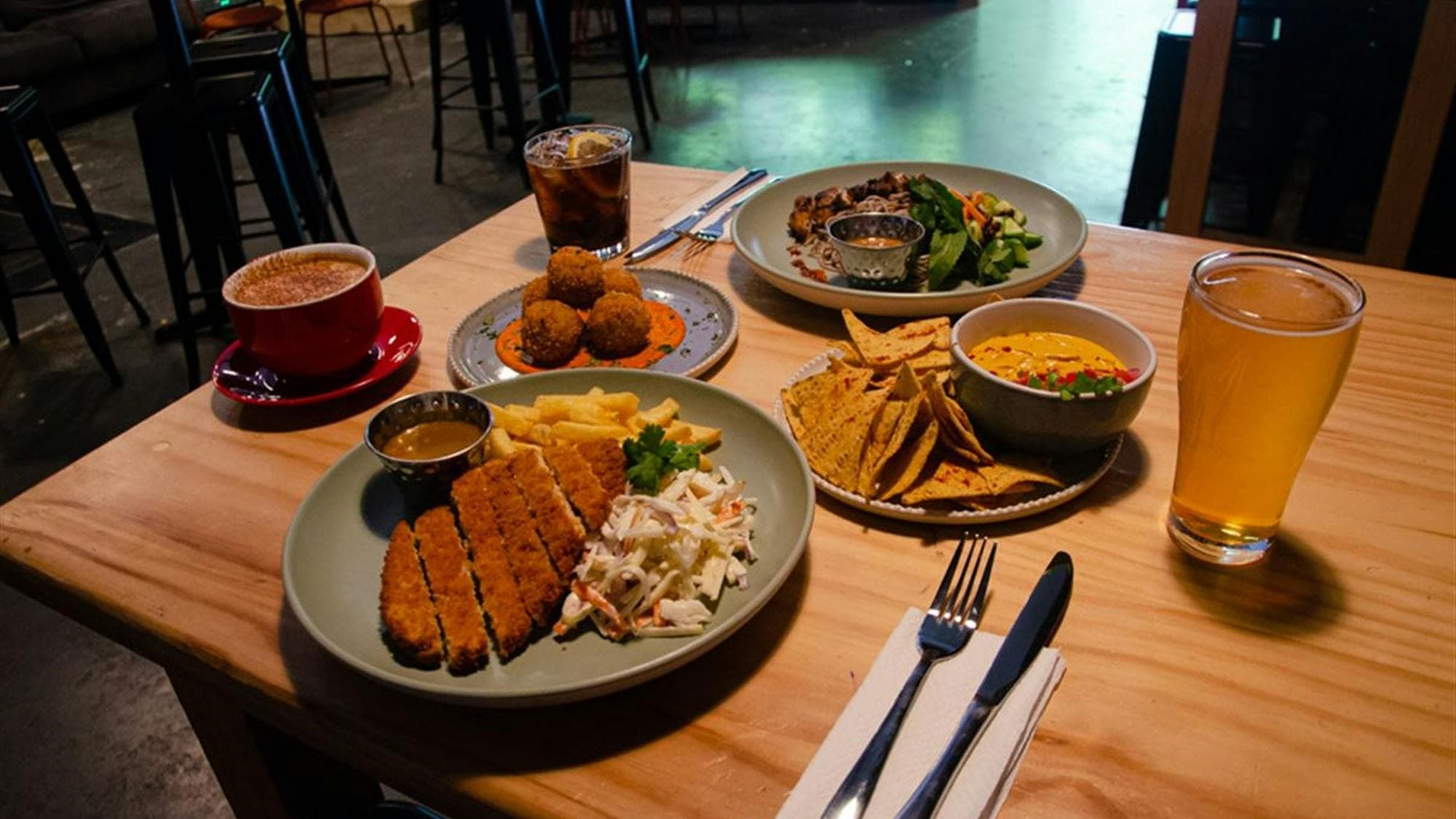 Variety of Dissent's food offerings set out on a wooden table. Arancini, schnitzel and corn chips.