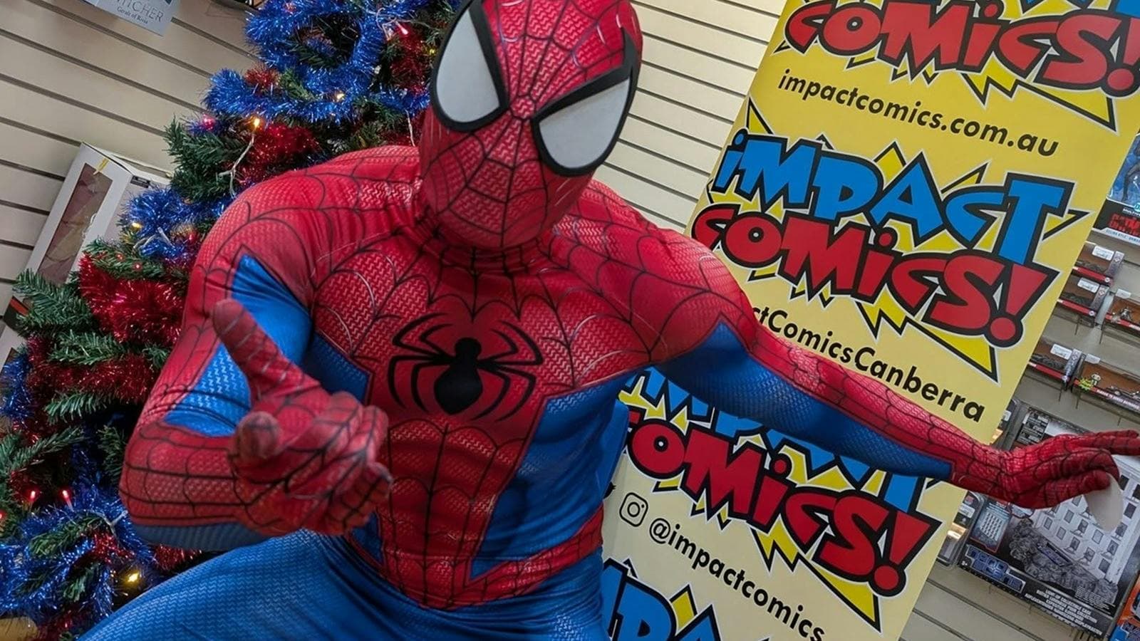 A man dressed as Spider-Man strikes a pose in front of a Christmas tree
