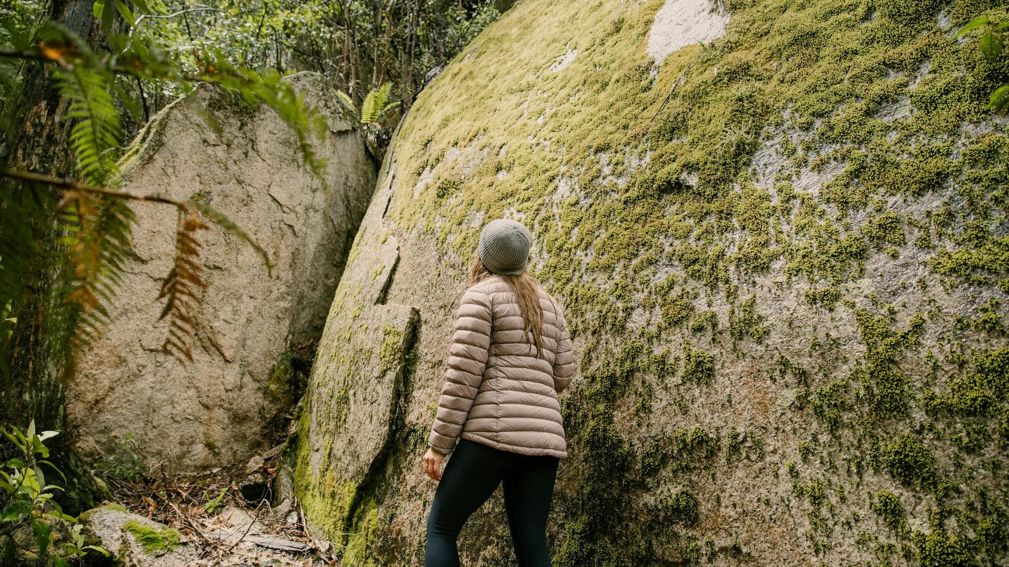 Woman hiking beside huge moss covered granite boulder