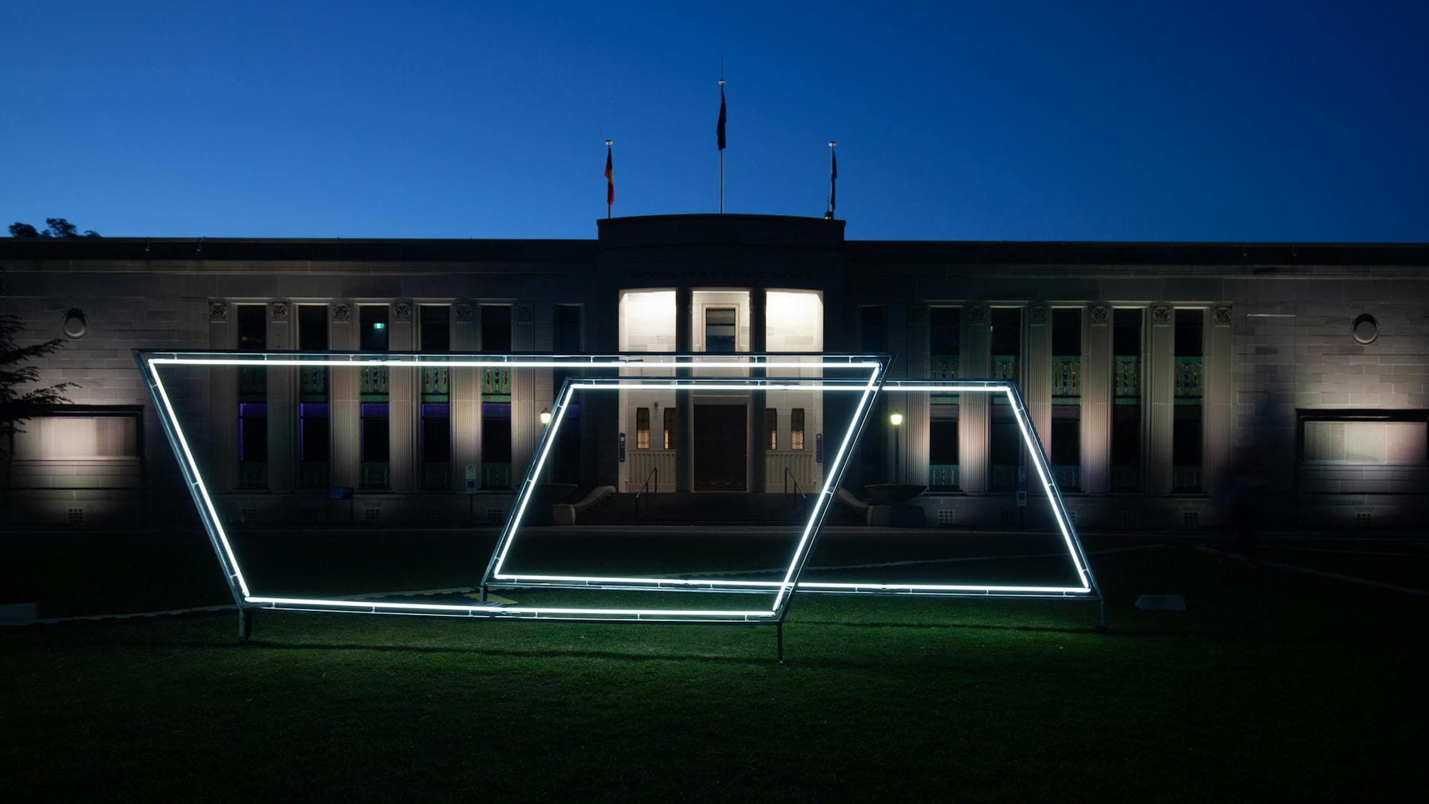 Neon light sculpture on the grass of the National Film and Sound Archive. Photo taken at night.