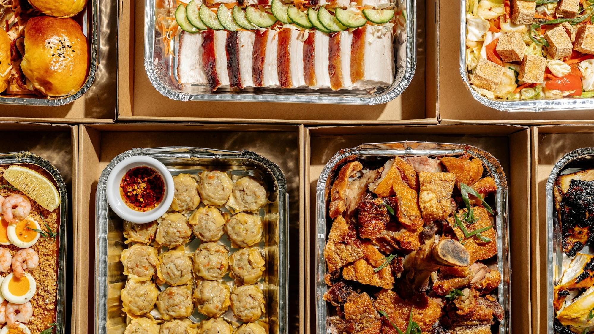 Assorted Filipino catering trays filled with roasted meats, buns, dumplings, seafood, salads and veg