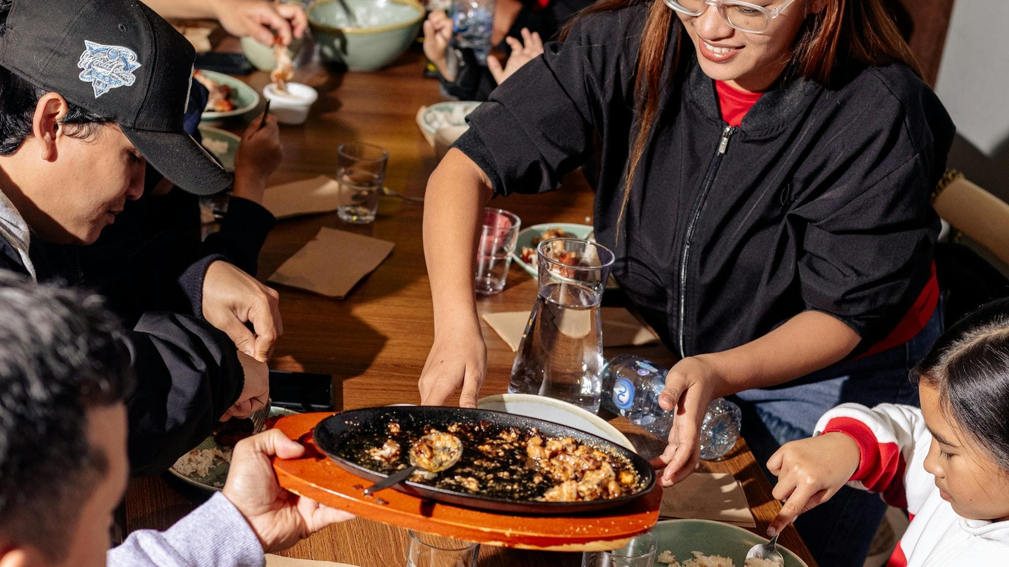 A group of people sitting around a dining table sharing Filipino dishes, with plates, bowls and drin