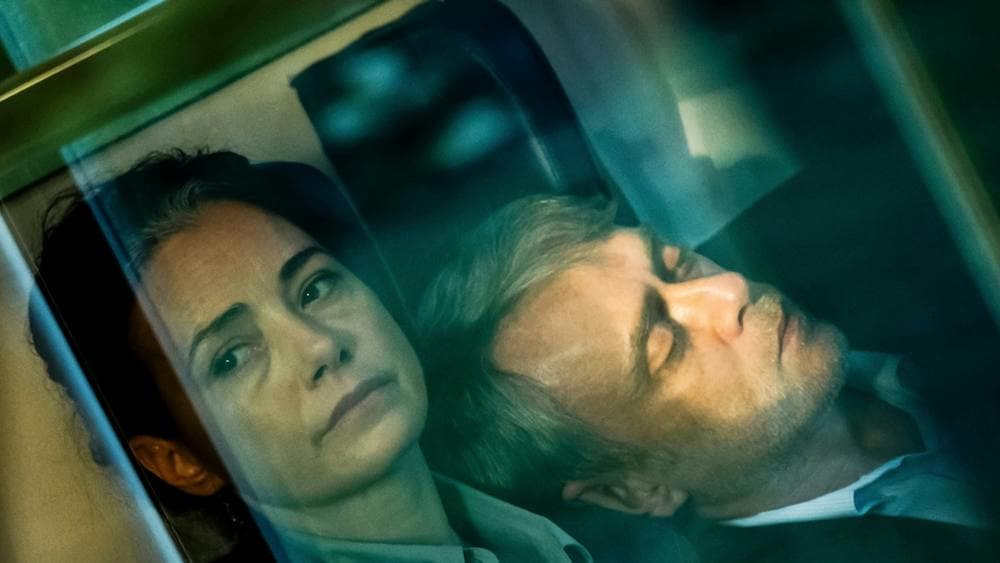 Hazy photo of woman looking morose past the camera and a man leaning on her shoulder