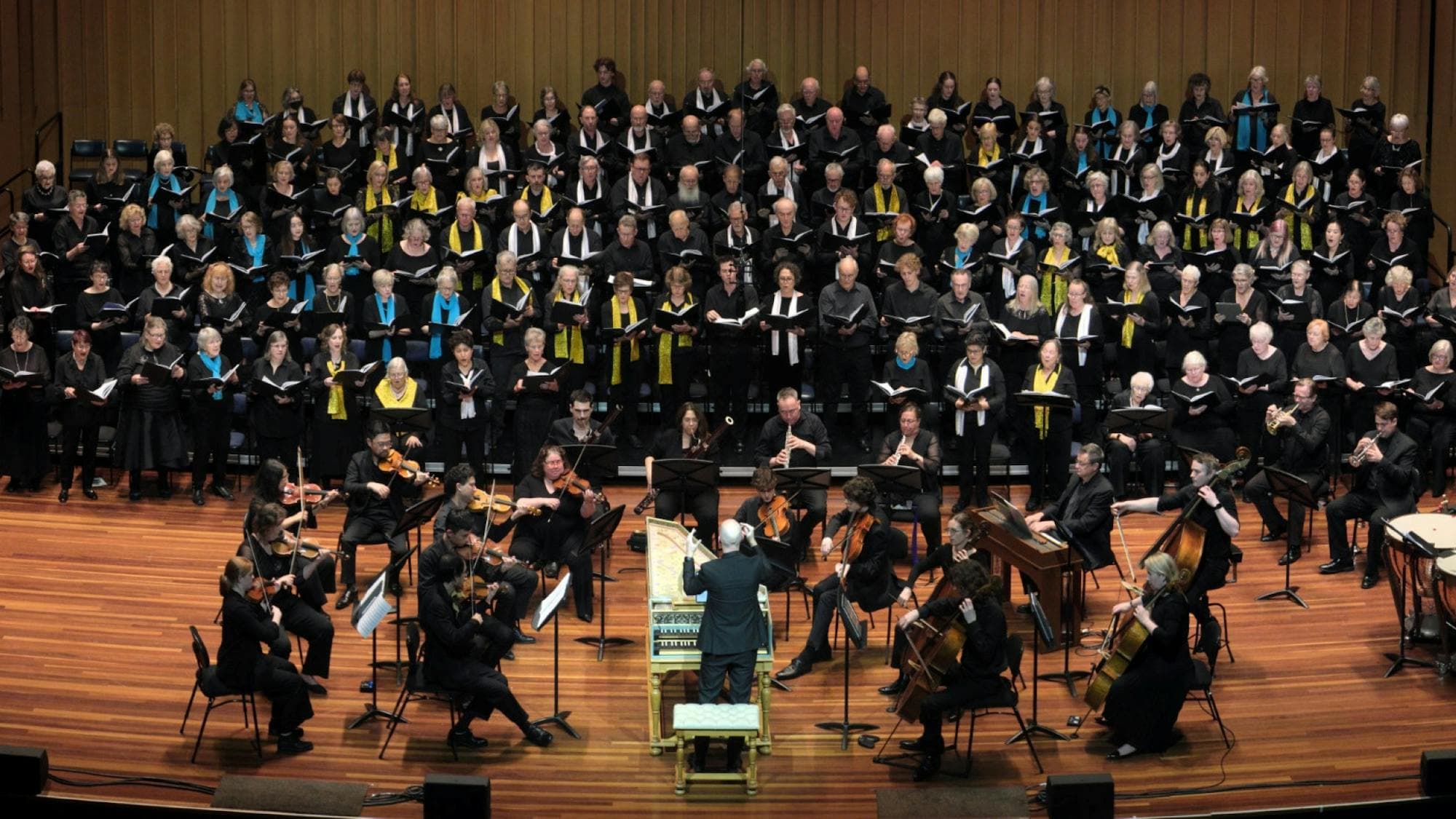 Choristers performing on stage with orchestra, conducted from a harpsichord by Erin Helyard